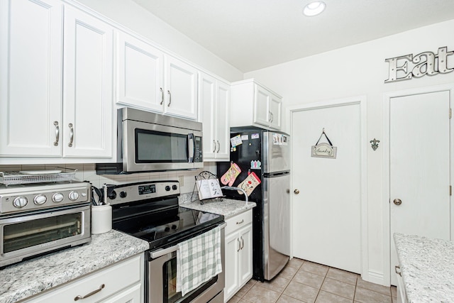kitchen with stainless steel appliances, light stone counters, white cabinetry, and light tile patterned flooring