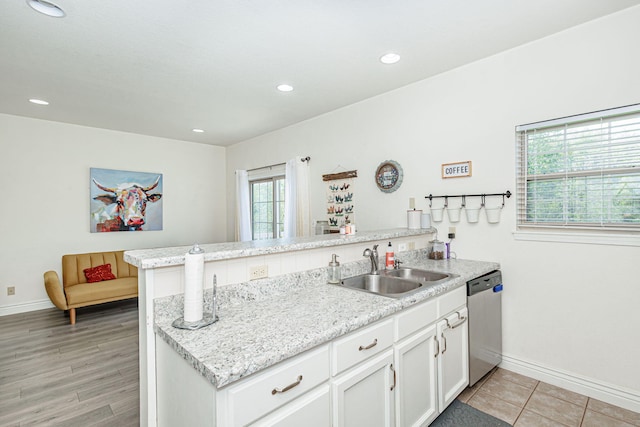kitchen with stainless steel dishwasher, a peninsula, baseboards, and a sink