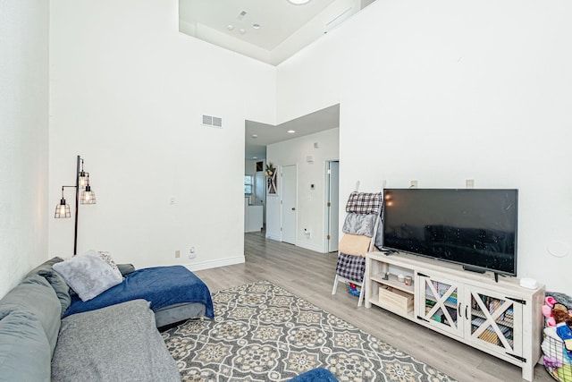 living room with visible vents, baseboards, a towering ceiling, and wood finished floors