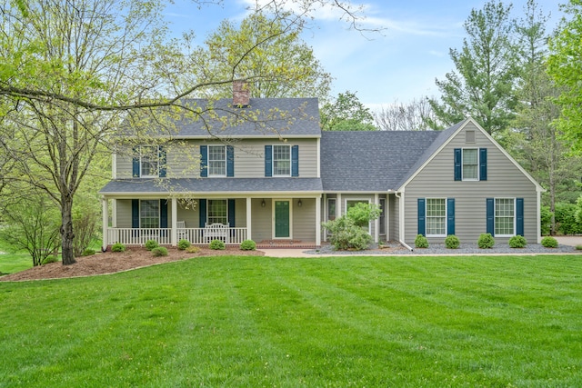 colonial house featuring a front yard, a shingled roof, covered porch, and a chimney