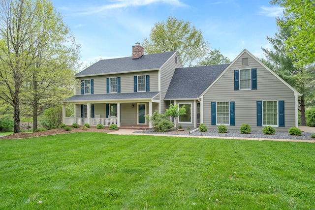 colonial-style house featuring a porch, a front yard, a shingled roof, and a chimney