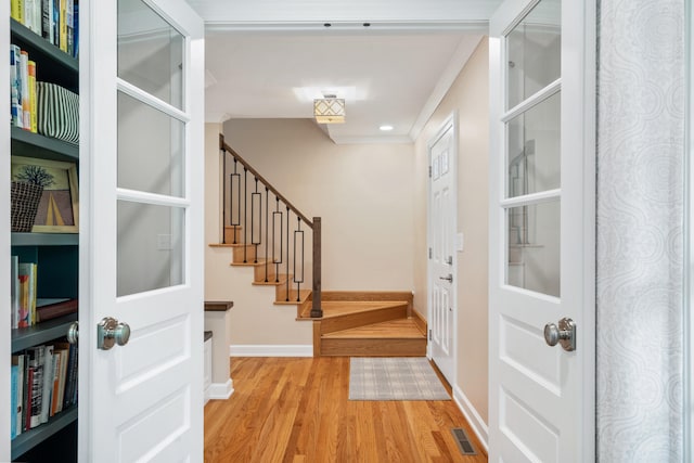 entrance foyer featuring visible vents, light wood-style floors, ornamental molding, baseboards, and stairway