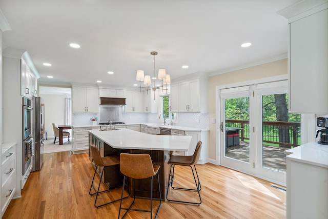 kitchen with decorative backsplash, a kitchen breakfast bar, light wood-style flooring, white cabinets, and an island with sink
