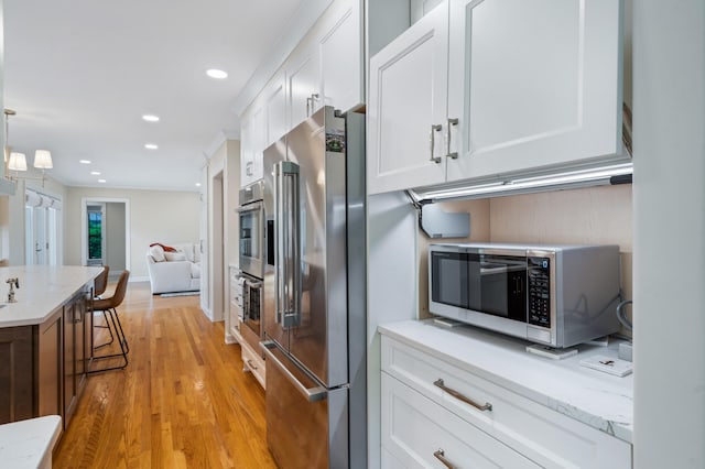 kitchen featuring recessed lighting, light stone counters, stainless steel appliances, white cabinets, and light wood finished floors