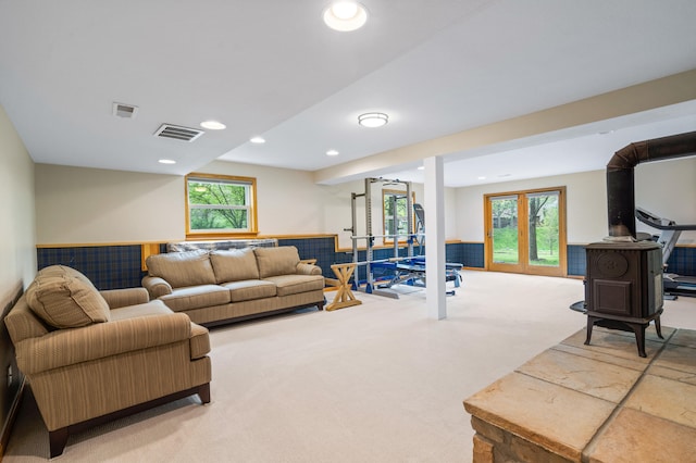 living room featuring a wood stove, visible vents, wainscoting, and carpet floors