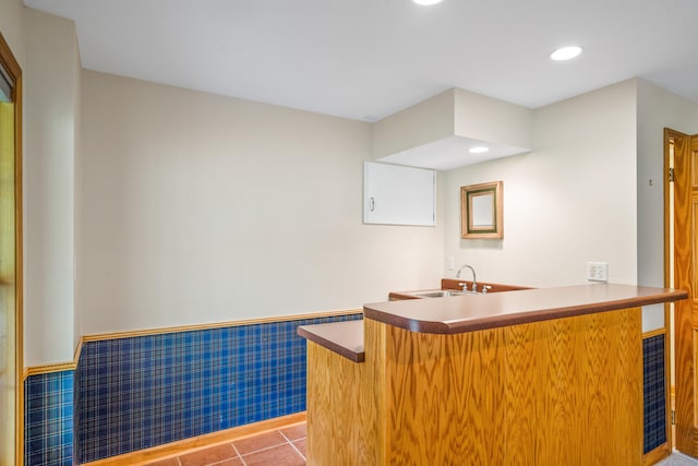 interior space with a sink, a breakfast bar area, a wainscoted wall, a peninsula, and tile patterned flooring