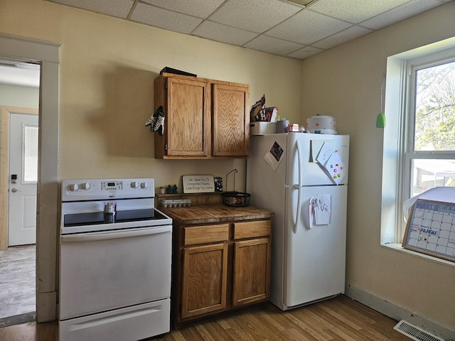 kitchen with dark countertops, visible vents, wood finished floors, white appliances, and brown cabinetry