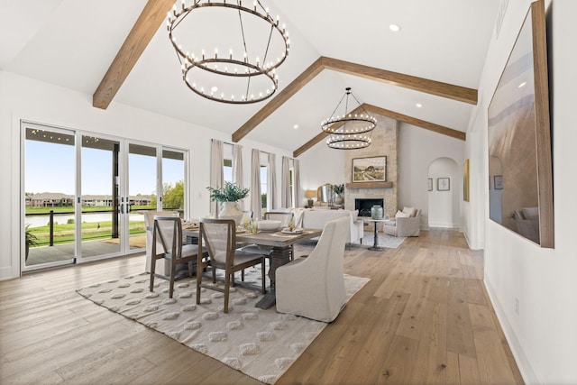 dining room with light wood-style flooring, a large fireplace, baseboards, beam ceiling, and an inviting chandelier