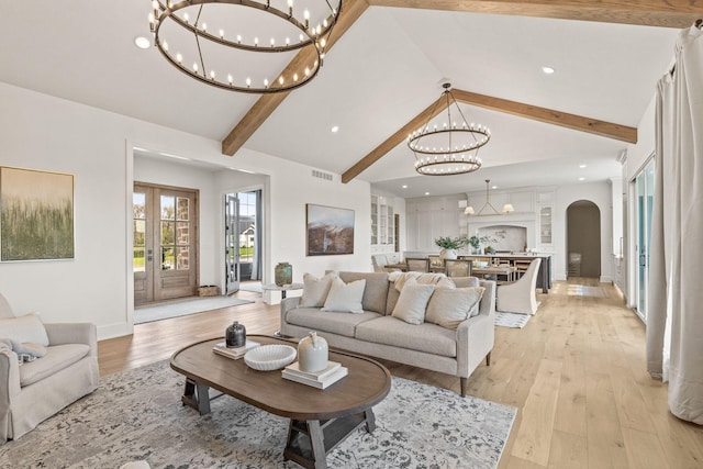 living area with beam ceiling, light wood-type flooring, arched walkways, and an inviting chandelier