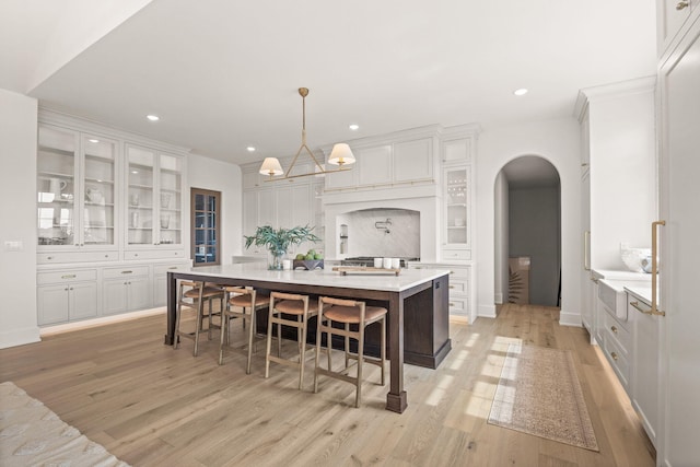 kitchen with white cabinetry, light wood-style floors, and arched walkways