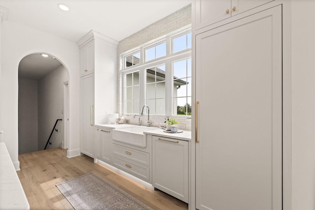 bar featuring arched walkways, a sink, light wood-style flooring, and plenty of natural light