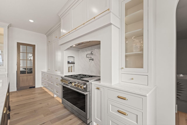 kitchen featuring glass insert cabinets, stainless steel range, light wood-style flooring, white cabinetry, and arched walkways