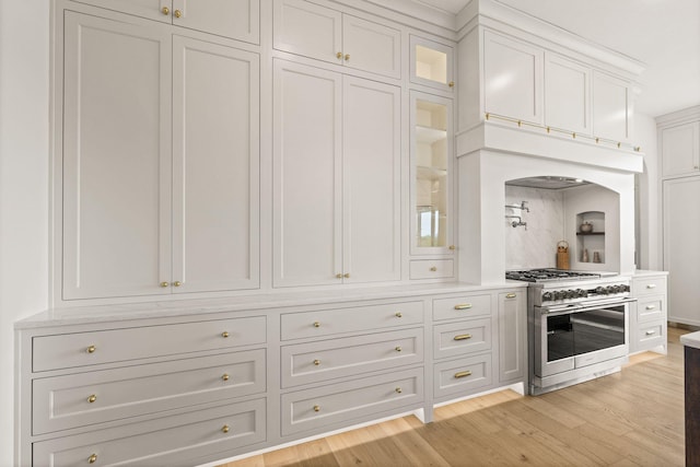 kitchen with arched walkways, glass insert cabinets, double oven range, light wood finished floors, and white cabinetry
