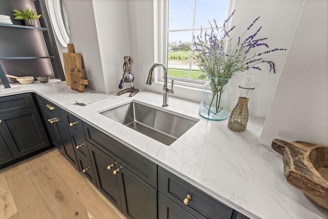 kitchen featuring light wood finished floors, open shelves, a sink, and light stone counters