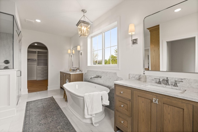 full bathroom with a stall shower, two vanities, a sink, and a freestanding bath