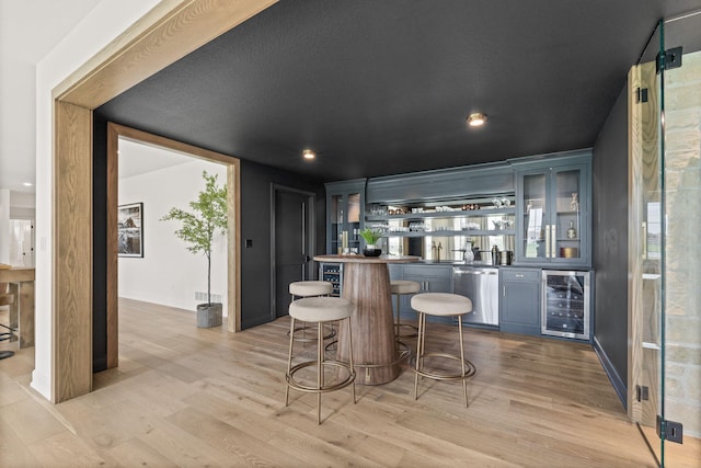 bar featuring stainless steel dishwasher, a sink, beverage cooler, light wood finished floors, and wet bar
