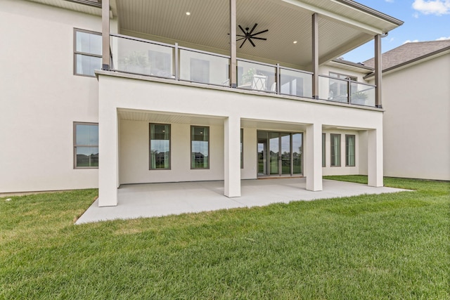 rear view of property featuring stucco siding, a balcony, and a lawn