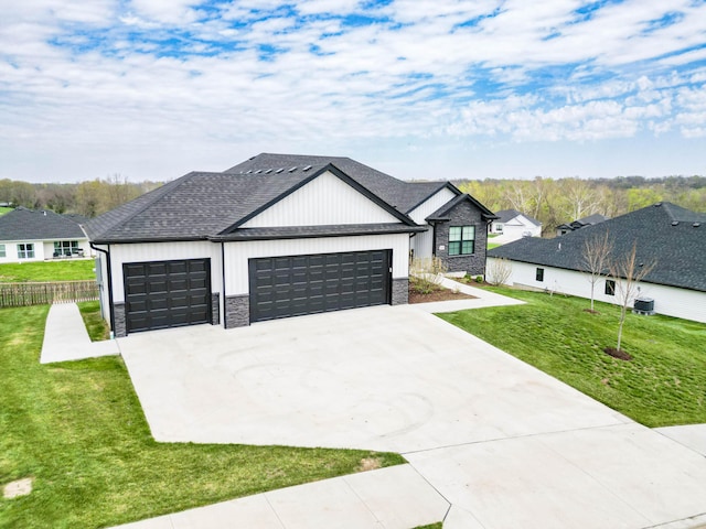modern farmhouse featuring a front yard, driveway, stone siding, an attached garage, and fence