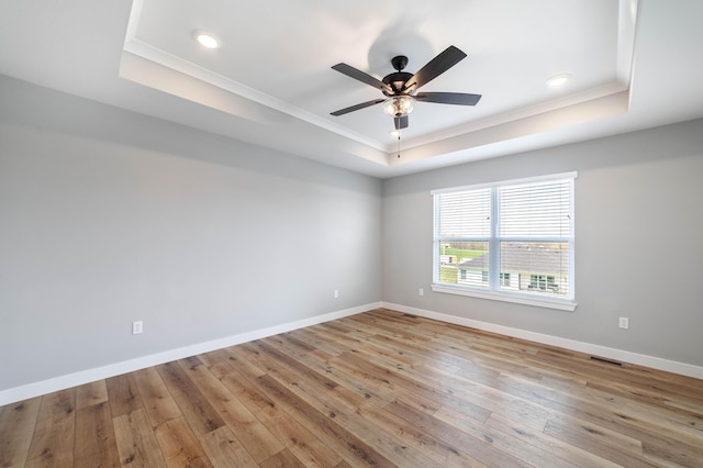 unfurnished room featuring crown molding, hardwood / wood-style flooring, a ceiling fan, and a raised ceiling