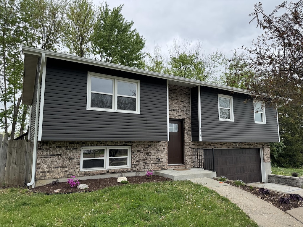 raised ranch with fence, driveway, brick siding, and a garage