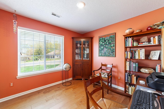 sitting room with baseboards, visible vents, a textured ceiling, and light wood-style flooring
