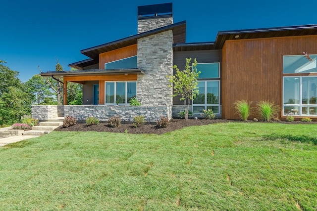 rear view of property featuring a yard, stone siding, and a chimney