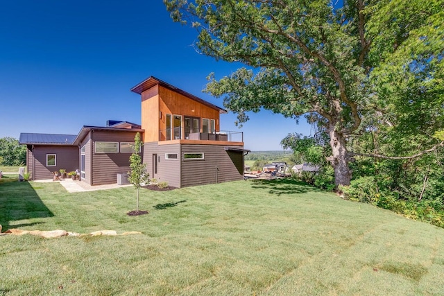 back of property featuring a balcony, a yard, and metal roof