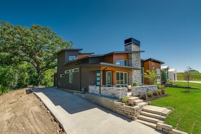 back of property featuring stone siding, concrete driveway, a yard, and a chimney