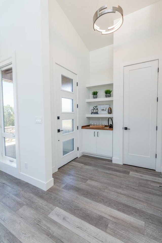 foyer entrance with light wood-style flooring, baseboards, a chandelier, and vaulted ceiling