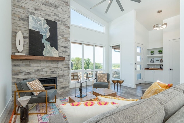 living room with wood finished floors, a fireplace, baseboards, ceiling fan, and a high ceiling