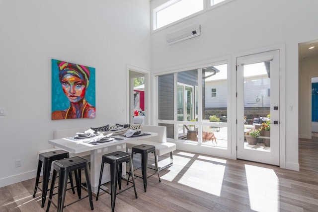 dining area featuring wood finished floors, baseboards, an AC wall unit, and a towering ceiling