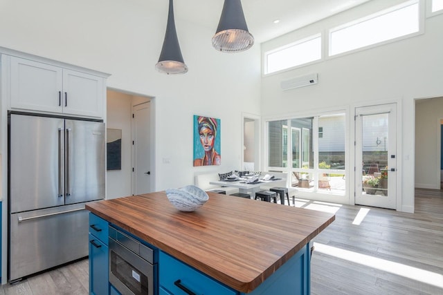 kitchen with high end fridge, wood counters, blue cabinetry, a wall unit AC, and a high ceiling