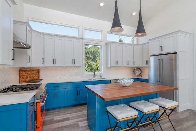 kitchen with high end appliances, a sink, butcher block countertops, blue cabinetry, and a breakfast bar area