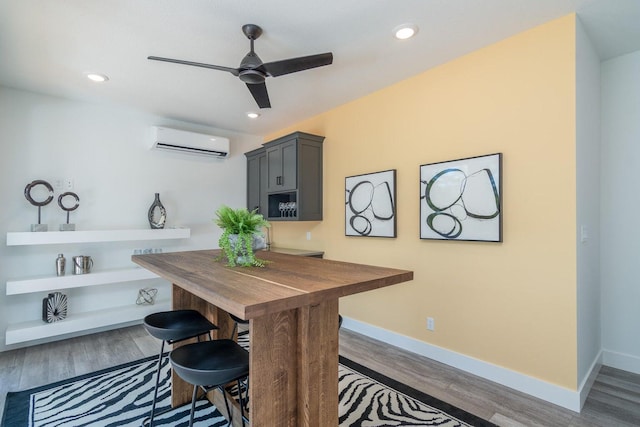 dining room with an AC wall unit, wood finished floors, ceiling fan, baseboards, and recessed lighting
