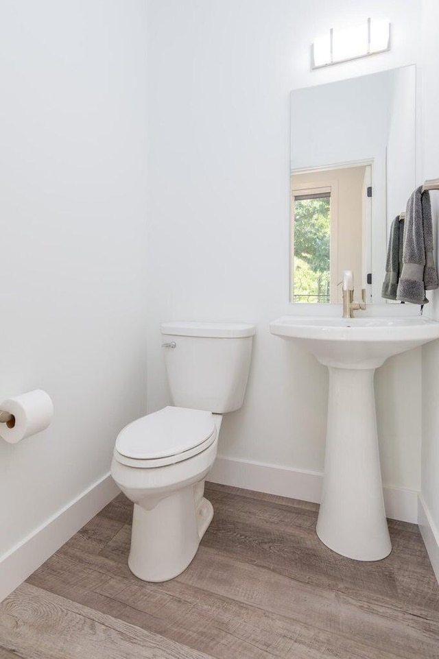 bathroom with toilet, baseboards, and wood finished floors