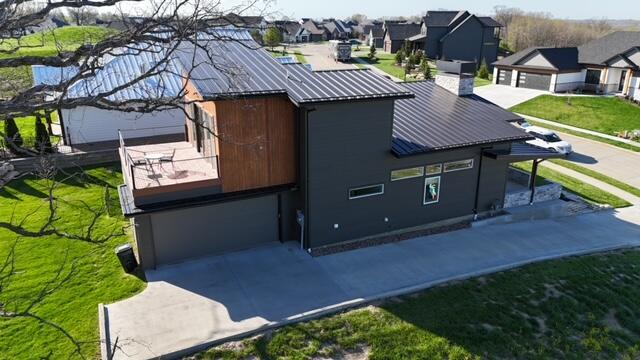 view of side of property featuring a garage, metal roof, a residential view, a standing seam roof, and driveway
