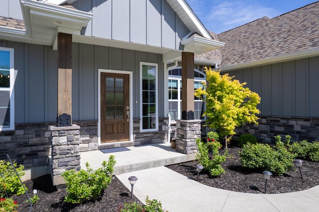 entrance to property with roof with shingles, board and batten siding, and stone siding
