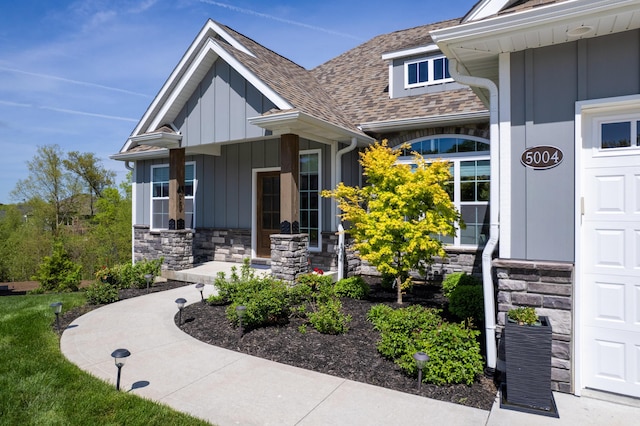 doorway to property with a shingled roof, board and batten siding, and stone siding
