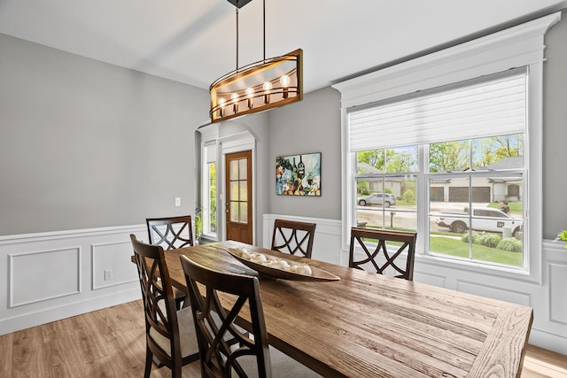 dining room with a wainscoted wall, a decorative wall, light wood finished floors, and arched walkways