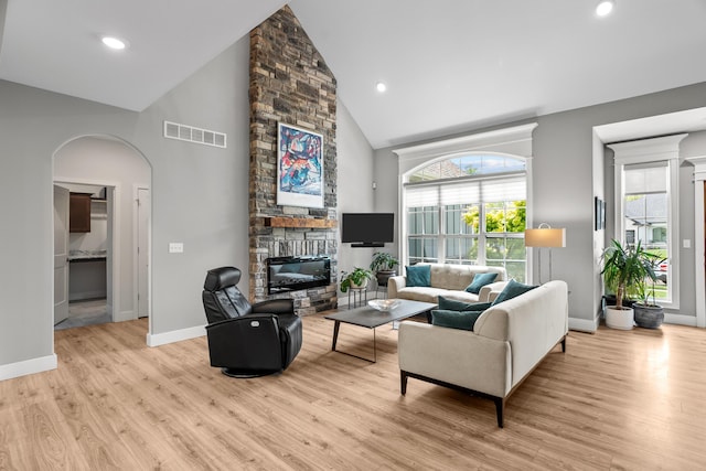 living area with a fireplace, arched walkways, high vaulted ceiling, light wood-type flooring, and visible vents