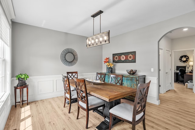 dining area featuring arched walkways, light wood-style flooring, and wainscoting