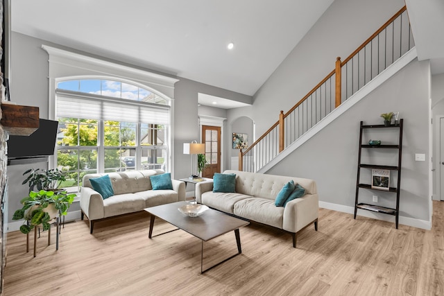 living area with recessed lighting, arched walkways, light wood-style flooring, and high vaulted ceiling