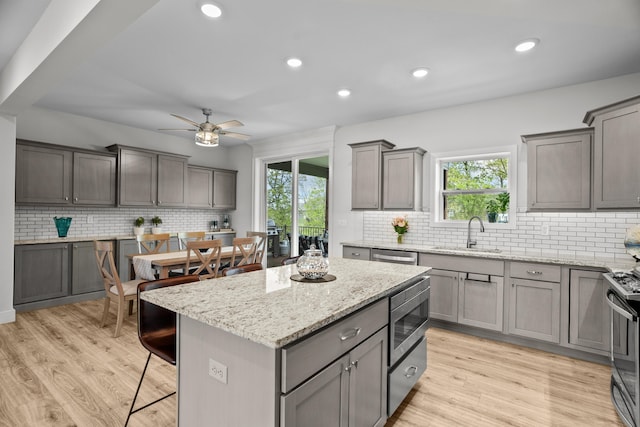 kitchen with ceiling fan, a breakfast bar area, backsplash, appliances with stainless steel finishes, and a sink