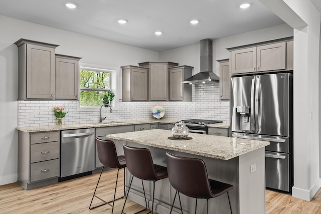 kitchen with a center island, light stone countertops, a sink, stainless steel appliances, and wall chimney exhaust hood