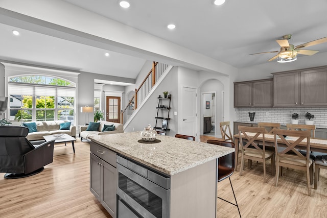 kitchen featuring open floor plan, a breakfast bar area, ceiling fan, stainless steel microwave, and backsplash