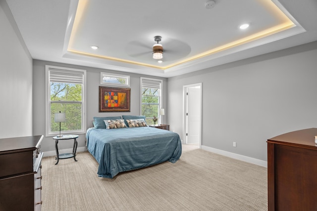 bedroom with a raised ceiling, baseboards, multiple windows, and light colored carpet