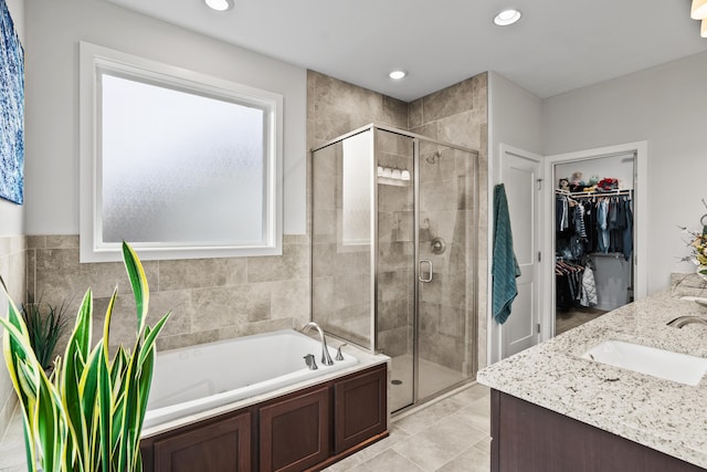 full bathroom with a sink, double vanity, a shower stall, a spacious closet, and a bath