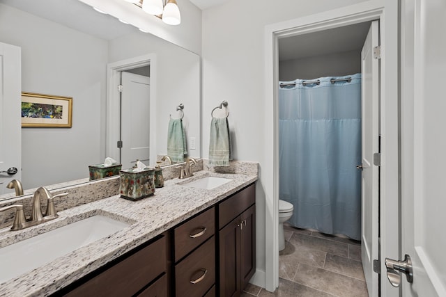 bathroom with double vanity, a sink, stone finish flooring, and toilet