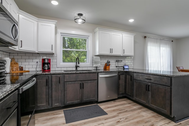 kitchen featuring stainless steel dishwasher, a peninsula, black electric range, a sink, and dark stone countertops
