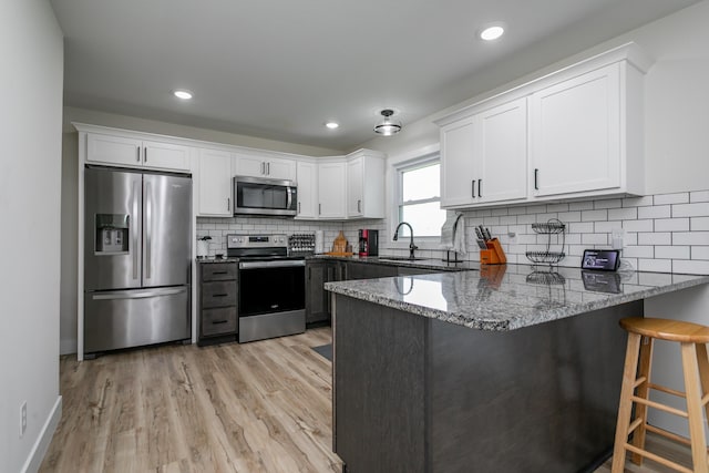 kitchen featuring appliances with stainless steel finishes, a sink, dark stone countertops, a peninsula, and white cabinetry